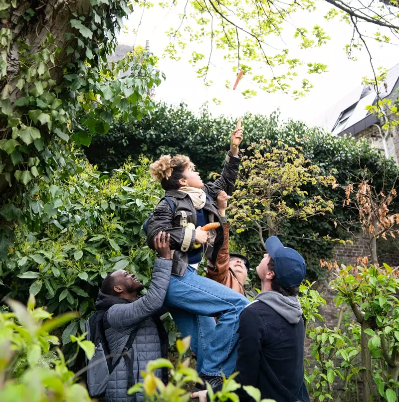 deux hommes portent une jeune fille pour qu'elle puisse décrocher une fleur d'un arbre