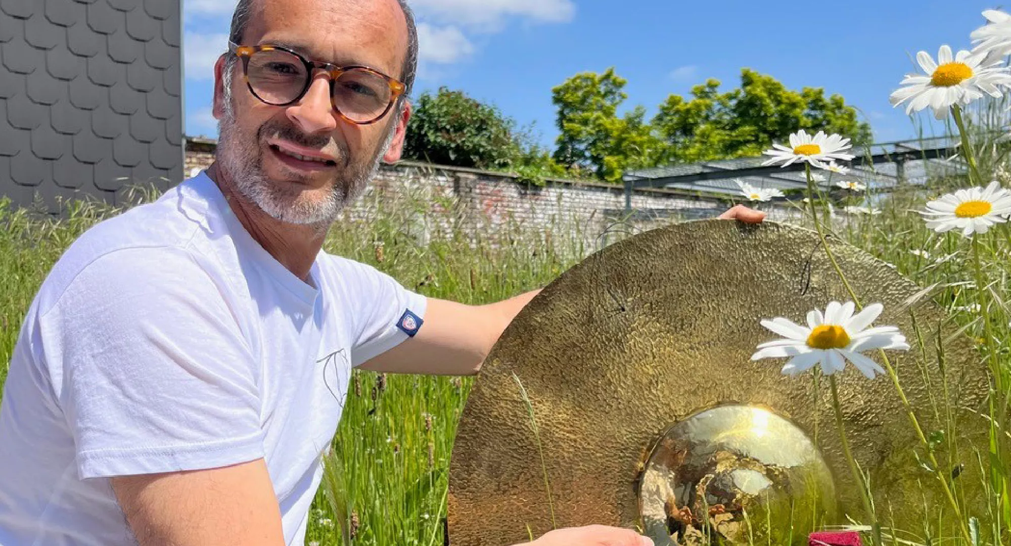 Jacques Pili assis dans l'herbe fleurie, une cymbale à la main