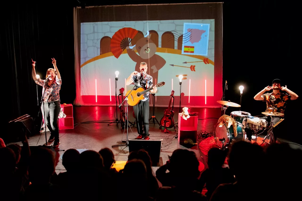 3 musiciens sur scène : une chanteur, un guitariste et un batteur. Une projection d'un dessin animé en fond de scène.