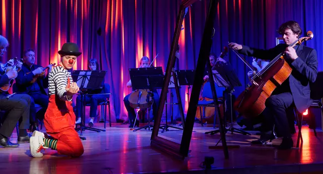 Photo d'un clown entouré de musiciens classiques