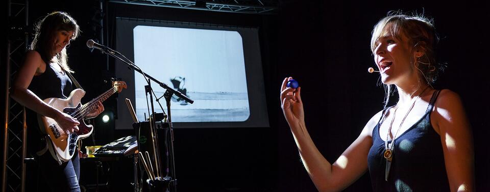 une chanteuse guitariste au premier plan, devant un écran de projection avec un dessin animé "félix le chat"