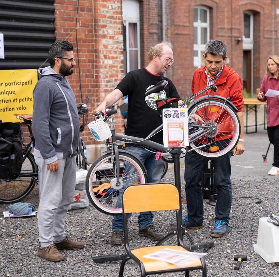 2 hommes participent à un atelier réparation de vélo dans la cour de la maison folie